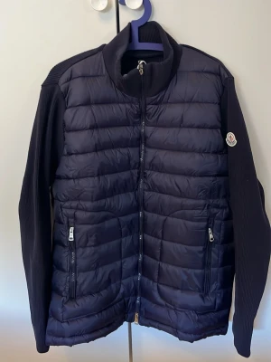 Mörkblå dunväst från Moncler - Snygg mörkblå dunväst från Moncler med quiltad front och ribbstickade ärmar. Västen har dragkedja framtill, två dragkedjefickor och en hög krage. Klassisk Moncler-logga på ena ärmen. Använd några gånger men passade inte mig så bra.Pris kan absolut diskuteras vid snabb affär 