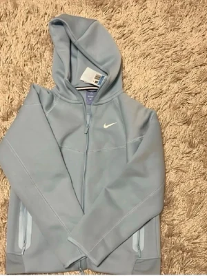 Nike NOCTA ljusblå Tracksuit - Säljer ett par ljusblå tracksuit från Nike NOCTA-kollektionen. Byxorna har raka ben, dragsko i midjan, dragkedjeförsedda fickor och diskreta loggor på benet. Perfekta för chill dagar eller när du vill ha en clean streetwear-look.