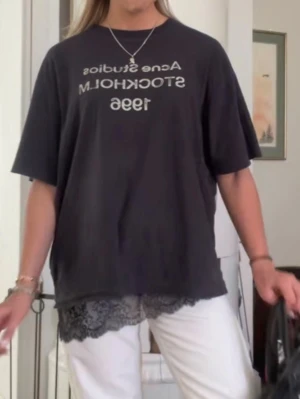 Svart Acne Studios t-shirt - Svart oversized t-shirt från Acne Studios med vit text 'Acne Studios Stockholm 1996' på bröstet. T-shirten har rund halsringning och korta ärmar. Materialet ser ut att vara mjuk bomull och nederkanten har en unik spetsdetalj.
