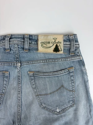 Ljusblå jeans från Jacob Cohen - Säljer ett par ljusblå jeans från Jacob Cohen med klassisk femficksdesign och snyggt broderad patch bak. Jeansen har raka ben och är tillverkade i mjukt denim-material som ger en avslappnad look.