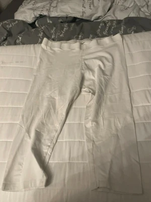 Vita leggings med hög midja - Ett par vita leggings med hög midja och stretchigt material. De har en enkel och klassisk design utan synliga detaljer eller mönster. Perfekta för en clean och stilren look. Den är 3/4