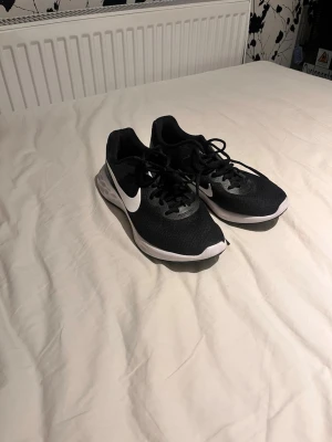 Svarta Nike sneakers med vit sula - Säljer ett par helt (OANVÄNDA) Snygga svarta Nike sneakers med vit sula och klassisk vit swoosh på sidan. Skorna har lågt skaft, snörning och ovandel i mesh för bra andningsförmåga. Perfekta för dig som gillar sportig och stilren look.