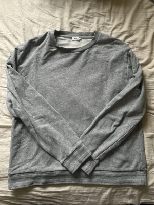 Grå långärmad tröja från Filippa K - En stilren grå långärmad tröja från Filippa K i mjukt bomullsmaterial. Tröjan har rund halsringning och en avslappnad passform, perfekt för en enkel och clean look.