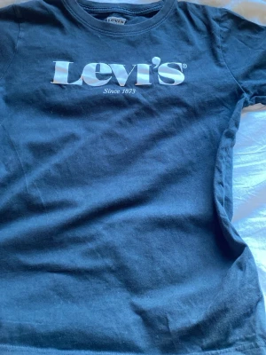 Svart Levi's t-shirt med logga - Svart t-shirt från Levi's med klassisk vit logga på bröstet. T-shirten har rund halsringning och korta ärmar. Tillverkad i mjuk bomull som är skön att bära. Perfekt för en avslappnad och stilren look.