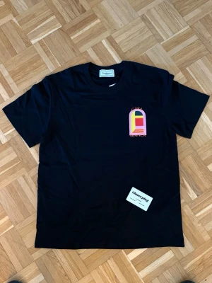 Svart t-shirt från Casablanca - Snygg svart t-shirt från Casablanca med färgglatt tryck på bröstet i rosa, gult, grönt och rött. Klassisk passform och rund halsringning. Perfekt för dig som vill ha en stilren men ändå unik look.