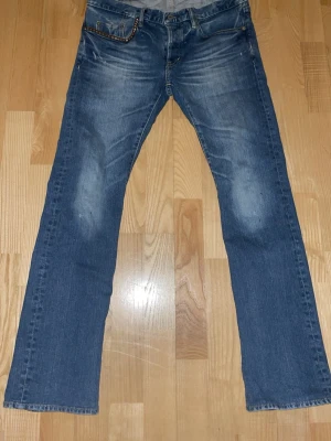 Hysteric glamour bootcut jeans - Säljer ett par klassiska blå bootcut jeans med snygga slitningar framtill. Jeansen har fem fickor, normal midja och är tillverkade i denim. Perfekta för en avslappnad och trendig look.