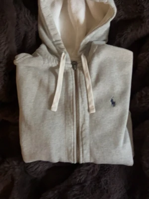 Ralph lauren zip hoodie - Grå ralph lauren zip hoodie som är storlek Medium och sitter lite lösare i passformen. Små defekter finns och syns på sista bilderna, men inget som påverkar utseende eller funktion.