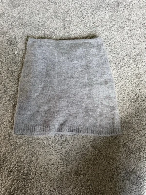 Grå stickad minikjol från Gina Tricot - Supermjuk och stilren grå stickad minikjol från Gina Tricot. Kjolen har en enkel, rak passform och ribbad kant nedtill. Perfekt att matcha med en oversized tröja eller boots för en trendig look.