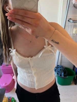 Topp - Beige/vit topp som passar perfekt till sommaren. Rosetter på båda banden och knappar i mitten. Använd endast en gång!