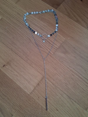 Silverfärgat lager-på-lager halsband - Trendigt silverfärgat halsband med flera lager, dekorerat med små runda plattor, en cirkel, en stjärnberlock och en lång hängande kedja. Perfekt accessoar för att lyfta din outfit med en modern touch.