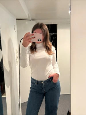 Vit polotopp med lång ärm - Klassisk vit polotopp med lång ärm och tight passform. Perfekt att styla med jeans eller kjol för en clean och enkel look. Tillverkad i mjukt material som känns skönt mot huden. Polokragen ger en trendig touch och passar till många olika outfits.