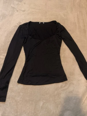 Svart långärmad topp med v-ringning - En svart långärmad topp med snygg v-ringning och figurnära passform. Perfekt att styla med jeans eller kjol för en clean look. Tunt och stretchigt material som känns skönt mot huden.