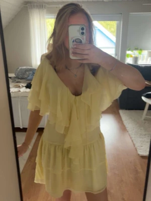 Ljusgul volangklänning med v-ringning - Söt ljusgul kortklänning med djup v-ringning och volangdetaljer både framtill och på ärmarna. Klänningen har en luftig passform och är tillverkad i ett tunt, lätt material som ger ett romantiskt intryck. Perfekt för varma dagar och somriga tillfällen. (aldrig använd)💓💓