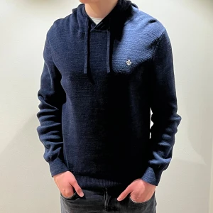 Mörkblå hoodie från Morris - Snygg mörkblå hoodie från Morris med dragsko i huvan och diskret logga på bröstet. Tillverkad i mjukt stickat material som ger en avslappnad men stilren look. Perfekt för dig som vill ha en hoodie med lite mer klass.