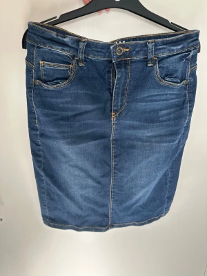 Blå jeanskjol med fickor från ONLY - Snygg blå jeanskjol i klassisk modell med fem fickor och kontrastsömmar. Kjolen har normal passform och stängs med knapp och dragkedja framtill. Perfekt till vardagslooken och enkel att matcha med olika toppar.