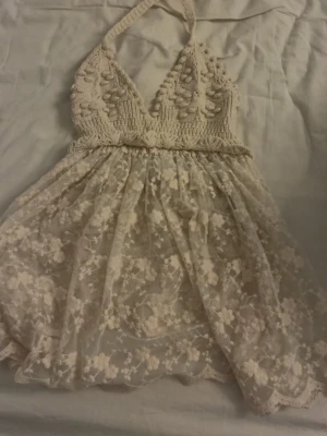Beige spetsnattlinne med virkad topp - Sött nattlinne i beige med virkad halterneck-topp och djup urringning. Kjoldelen är i transparent spets med blommigt mönster och vågig kant. Perfekt för dig som gillar romantisk och bohemisk stil. Köpt ifrån Zara är i storlek xs den är aldrig använd köpt för 499kr men säljer för 399kr pris kan diskuteras så man kan säga att den är helt ny fast utan prislapp 