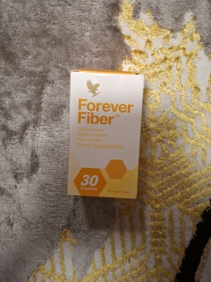 Forever Fiber kosttillskott 30 st - Forever Fiber är ett glutenfritt kosttillskott med 30 portionspåsar. Innehåller akaciagummi, majsfiber, dextrin och fruktooligosackarider. Förpackningen är vit och gul med hexagonmönster och text i orange.