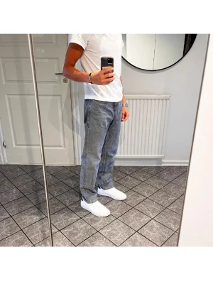 Grå raka jeans i klassisk modell - Säljer ett par grå jeans med rak passform och normal midja. Jeansen har en klassisk femficksdesign och är tillverkade i denim. Perfekta för en avslappnad och stilren look.