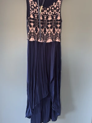 Marinblå långklänning från Oasis - Snygg marinblå långklänning från Oasis med spetsdetaljer i svart och nude upptill. Tillhörde skärp. Klänningen har ärmlös design och ett flytande, asymmetriskt fall. Perfekt för dig som vill ha en unik och elegant look.