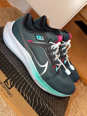 Nike svart-turkos sneakers med rosa detaljer - Snygga Nike Pegasus sneakers i svart mesh med turkosa och vita detaljer samt rosa accenter. Storlek 41 . -Pris 249kr