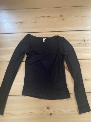 Svart långärmad topp med urringning och spets längst kanten - Svart långärmad topp från Nelly med söt spetskant vid halsringningen. Enkel och stilren design som funkar till många looks.