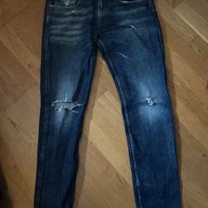Replay anbbas med slitningar  - Säljer ett par blå jeans från replay med snygga slitningar och hål på benen. Klassisk femficksmodell med raka ben och normal midja. Jeansen har en cool tvättad look och är tillverkade i bomull. Perfekta för en avslappnad och trendig stil.