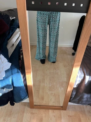 Mönstrade vida leggings i turkos - Säljer ett par snygga leggings med turkost och vitt diamantmönster. De har en lös och vid passform med resår i midjan för extra komfort. Perfekta för dig som gillar färg och mönster! Materialet känns mjukt och stretchigt.
