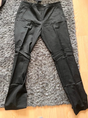 Svarta kostymbyxor - Snygga svarta kostymbyxor med smal passform och pressveck. Byxorna har diskreta fickor fram och är tillverkade i ett mjukt, stretchigt material som ger en clean och modern look. Perfekta för dig som vill ha en stilren vibe.