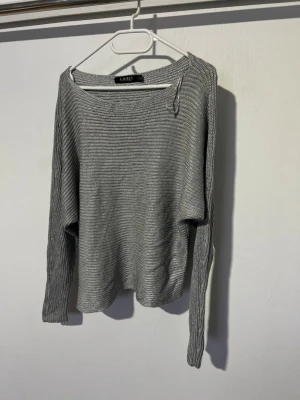 Grå stickad tröja från Lauren Ralph Lauren - Snygg grå stickad tröja från lauren Ralph lauren med rund halsringning och långa ärmar. Tröjan har en avslappnad passform och är tillverkad i ett mjukt, tunt stickat material som passar perfekt till alla tillfällen.