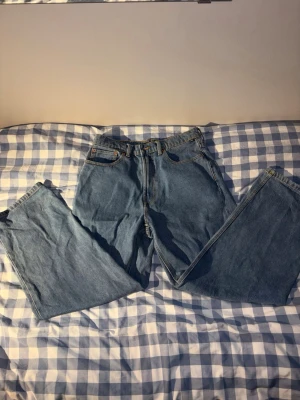 Blå raka Vans jeans - Klassiska blå Vans jeans med rak passform och hög midja. Jeansen har fem fickor, bälteshällor och en brun läderpatch bak i midjan. Tillverkade i slitstark denim som ger en tidlös look. Perfekta för dig som gillar vintage vibe och enkel stil. Observera att de är väldigt baggy!