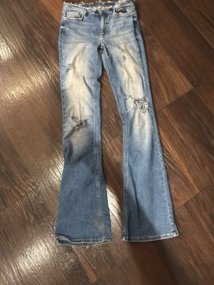 Ljusblå bootcut jeans med slitningar - Säljer ett par otroligt snygga ljusblå bootcut jeans med slitna detaljer och hål på knäna. Har själv gjort hålen och det slitna vid midjan. Storlek 32, jag som vanligtvis har storlek 164 passar perfekt i dom. Vet ej vart dom är ifrån från början!