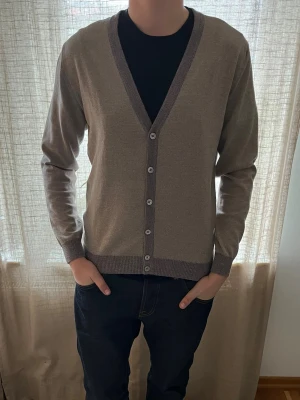 Stenströms Beige kofta med knappar - Säljer en stilren beige kofta med v-ringning och knäppning framtill. Koftan har ribbade muddar och kant, samt kontrasterande mörkare kant längs v-ringningen. Perfekt för lager-på-lager och passar till det mesta. Är storlek L men sitter mer en M/L. Endast använd 1-2 gånger dvs i princip helt ny. Hör av er vid frågor eller funderingar! 💛