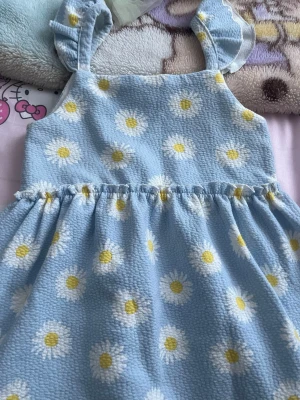 Blå klänning med prästkragar och volang - Ljusblå kortklänning med vita och gula prästkragar, volangprydda axelband och rynkad midja. Tillverkad i ett mjukt, strukturerat tyg som känns bekvämt och ger en söt och somrig vibe.