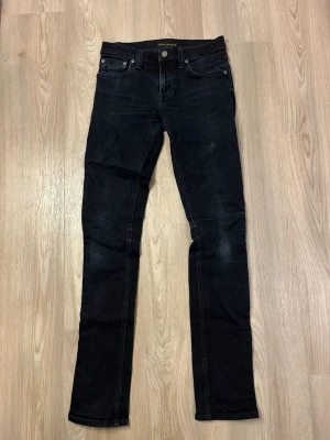 Nudie Jeans  - Tja! Säljer nu ett par Nudie jeans i storlek W27, L34. Jeansen är sjukt snygga då de är svarta men i vissa ljus är de lite mörkblåa, sjukt unikt enligt mig. De är i väldigt fint skick och använt sparsamt. Modellen heter Tube Kelly Tveka inte på att höra av dig vid frågor och funderingar  Priset är som vanligt diskuterarbart  Skickar alltid inom 24 timmar