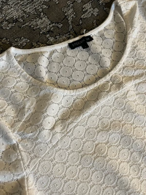 Vit spetsblus från Stockh LM - Säljer en vit blus från Stockh LM med rund halsringning och ett fint spetsmönster i cirklar. Blusen har en elegant och feminin look med genombruten spets och mjukt tyg. Perfekt att styla med jeans eller kjol för en trendig outfit.