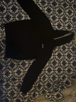 Svart hoodie från JD  - Säljer en svart hoodie från JD med dragkedja och huva. Klassisk design med logotyp på bröstet och mjukt material som känns skönt mot huden. 