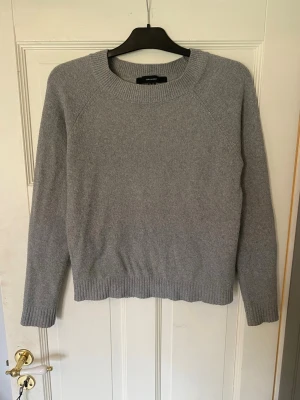 Grå stickad tröja från Vero Moda  - En stilren grå stickad tröja från Vero Moda i mjukt material. Tröjan har rund halsringning, långa ärmar och ribbade muddar vid ärmslut och nederkant. Perfekt för lager på lager och enkel att matcha med olika outfits.