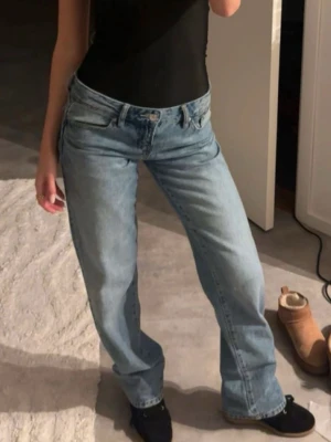 Ljusblå raka jeans - Säljer ett par ljusblå jeans med rak passform och klassisk femficksdesign. Jeansen har låg midja och är tillverkade i ett slitstarkt denimtyg. Perfekta för en avslappnad och trendig look.