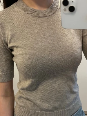 Beige stickad tröja/t-shirt från NA-KD - Säljer en stilren beige stickad tröja från NA-KD. Tröjan har rund halsringning, ribbade muddar och korta ärmar. Perfekt att matcha med jeans eller kjol för en enkel och snygg look.