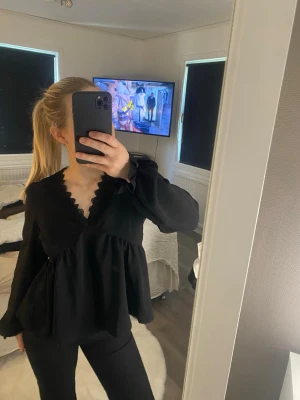 Svart v-ringad blus med volang - Snygg svart blus med v-ringning och volangkant längs urringningen. Blusen har långa ärmar och en lös, flowy passform som ger en avslappnad men chic look😊