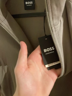 Beige ziptröja från BOSS Homewear - Snygg beige loungewear-ziptröja från BOSS Homewear med broderad logga på bröstet. Tröjan har dragkedja framtill och är perfekt för en avslappnad stil hemma. Mjukt material och klassisk design.