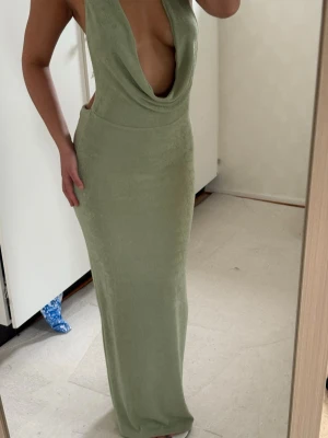 Ljusgrön långklänning med djup urringning - Trendig ljusgrön långklänning med djup draperad urringning och halterneck. Klänningen är ärmlös och har en smickrande, figurnära passform. Perfekt för dig som vill sticka ut med en elegant och modern look.