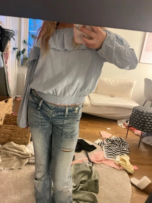 Ljusblå offshoulder blus med volang från H&M - Säljer en ljusblå offshoulder blus med bred volang runt axlarna och smockad midja. Blusen har långa ärmar.🩵