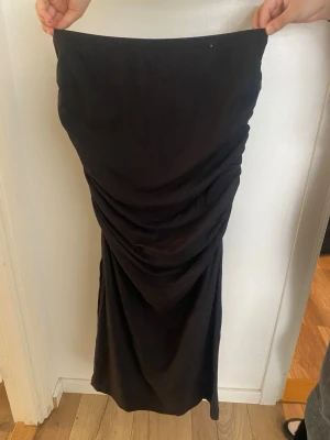 Svart långkjol med drapering - Säljer en svart långkjol med snygg drapering framtill. Kjolen har en enkel men elegant look och är perfekt för dig som gillar stilrena plagg med en twist. Materialet känns mjukt och följsamt mot kroppen.