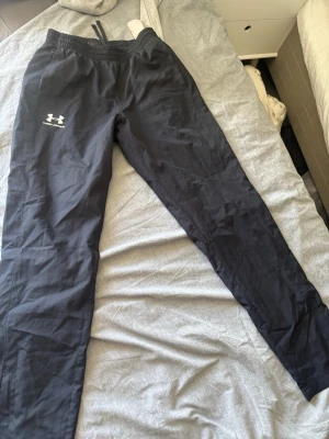 Svarta träningsbyxor Under Armour - Säljer ett par svarta träningsbyxor från Under Armour med resår i midjan och dragsko. Byxorna har två sidofickor och logga i vitt på vänster lår. Perfekta för gymmet eller löprundan.