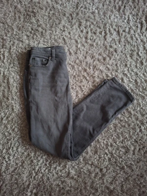 Gråa Jack&Jones slim fit jeans - Snygga gråa Jack&Jones slim fit jeans med klassisk femficksdesign och normal midja. Jeansen har raka ben och är tillverkade i ett mjukt denimtyg som ger en skön känsla. Perfekta för dig som gillar en enkel och stilren look.