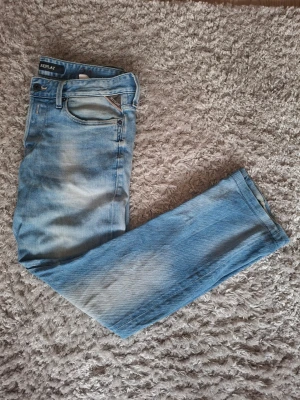 Ljusblå Replay jeans herr - Snygga ljusblå jeans från Replay med klassisk femficksmodell och slitna detaljer. Jeansen har raka ben och normal midja. Materialet är mjukt denim som ger en avslappnad look. Perfekta för dig som gillar en casual stil.