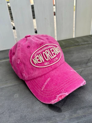 Vintage retro distressed Rosa keps med New Orleans-brodyr - Snygg rosa keps med broderad text 'NEW ORLEANS' och 'LET THE GOOD TIMES ROLL' framtill. Kepsen har en vintage look med slitna detaljer och böjd skärm. Tillverkad i bomullstyg och justerbar baktill för perfekt passform.