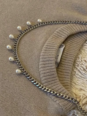 Silverfärgat halsband med pärlor - Säljer ett snyggt halsband i silverfärgad metall med kedjedesign och vita pärlor som hänger längs hela halsbandet. Perfekt för dig som vill ha en trendig accessoar med lite extra edge och detaljer.