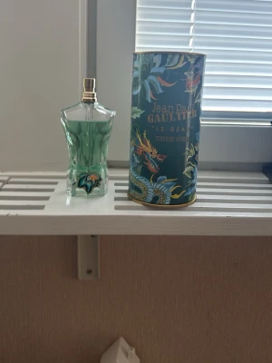 Jean Paul Gaultier Le Beau Paradise - Jean Paul Gaultier Le Beau Paradise är en parfym i en unik, kroppsliknande glasflaska med grön ton. Förpackningen är dekorerad med färgstarka tropiska motiv och drakar. Flaskan har gulddetaljer och en elegant design som sticker ut i badrumshyllan.